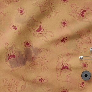 May include: A brown fabric with a repeating pattern of a spooky, red-toned monster with a skull and crossbones, and a red eye. There are also safety pins and a black spool on the fabric.