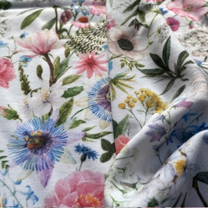 May include: White fabric with a floral print featuring pink, blue, and yellow flowers. The fabric is soft and has a subtle sheen.