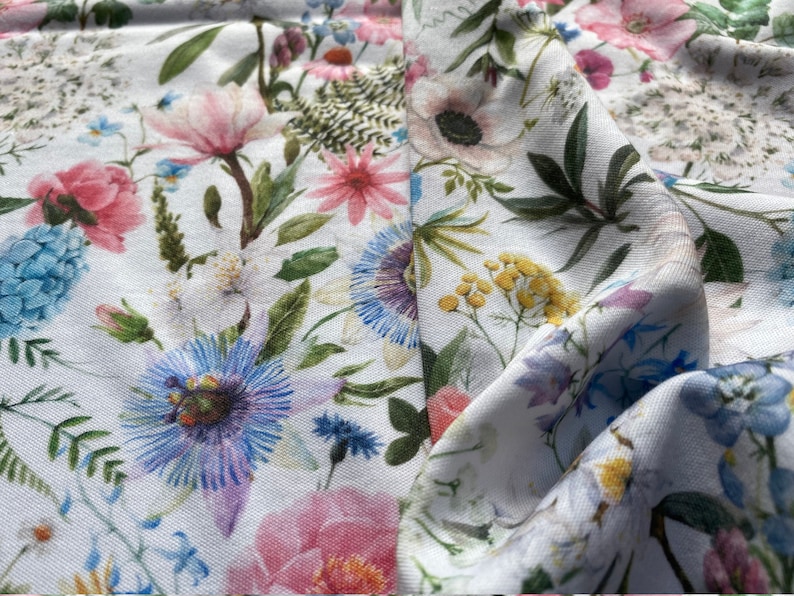 May include: White fabric with a floral print featuring pink, blue, and yellow flowers. The fabric is soft and has a subtle sheen.