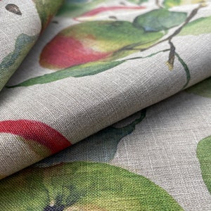 May include: Close-up of a fabric with a printed design of green leaves and red apples. The fabric has a textured, linen-like appearance.