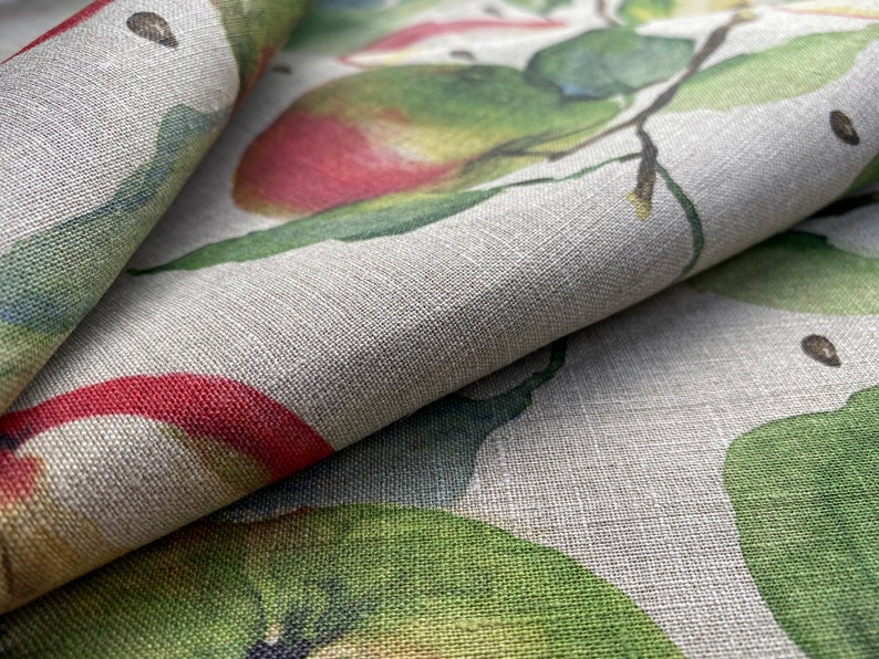May include: Close-up of a fabric with a printed design of green leaves and red apples. The fabric has a textured, linen-like appearance.