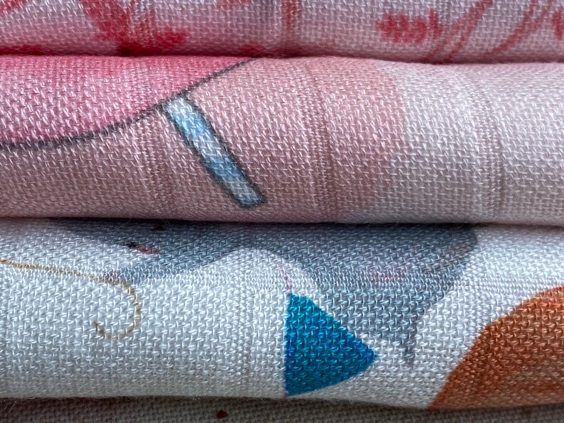 K&ouml;nnte beinhalten: Ein Stapel aus drei weichen, gewebten Babydecken. Die obere Decke ist rosa mit einem wei&szlig;en und blauen Design. Die mittlere Decke ist wei&szlig; mit einem grauen, blauen und orangefarbenen Design. Die untere Decke ist wei&szlig; mit einem goldenen Design.