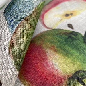 May include: Close-up of a fabric with a repeating pattern of red, green, and yellow apples. The fabric has a linen texture.