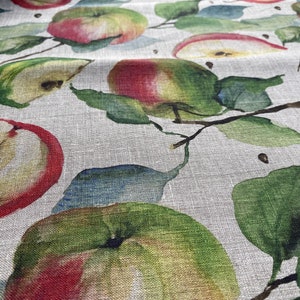 May include: A close-up of a fabric with a watercolor pattern of red and green apples and leaves on a light beige background.