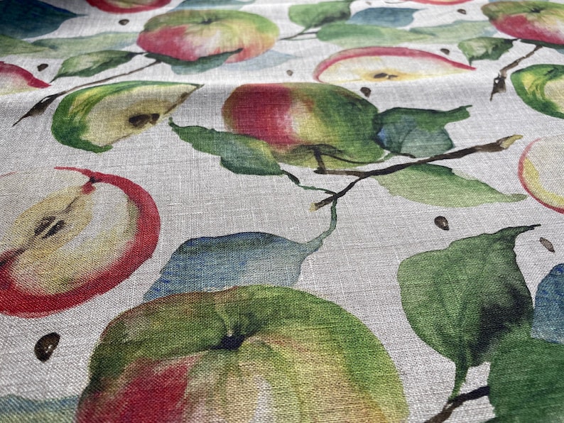 May include: A close-up of a fabric with a watercolor pattern of red and green apples and leaves on a light beige background.