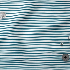 May include: A white and teal striped fabric with a black spool of thread, safety pins, and a button.
