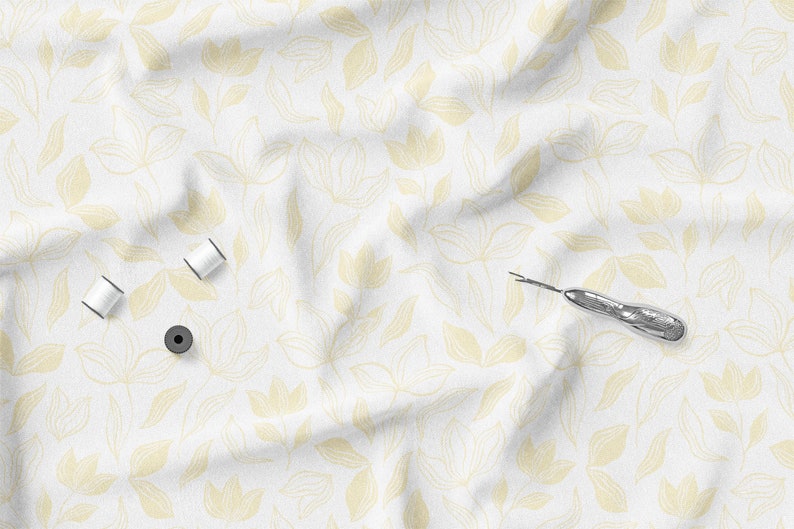 K&ouml;nnte beinhalten: Ein wei&szlig;er Stoff mit gelbem Blumenmuster, mit drei Spulen wei&szlig;en Fadens, einem schwarzen magnetischen Nadelkissen und einem silbernen Nahttrenner. Der Stoff ist leicht zerknittert, was darauf hindeutet, dass es sich um einen Stoff zum N&auml;hen oder Basteln handelt.