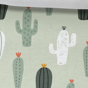 May include: A green and white cactus print fabric with a repeating pattern of different types of cacti. The fabric is 25 inches wide.