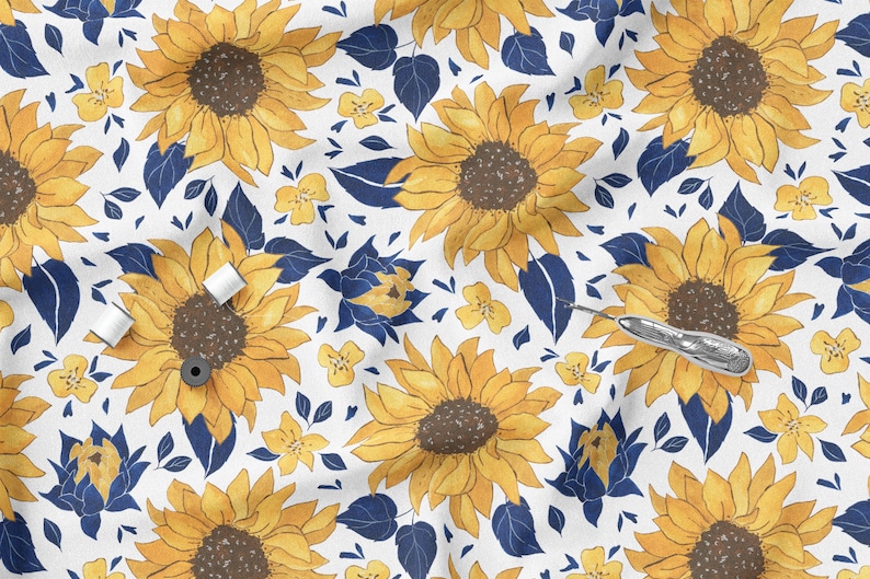 K&ouml;nnte beinhalten: Wei&szlig;er Stoff mit einem sich wiederholenden Muster aus gelben Sonnenblumen, kleinen gelben Blumen und marineblauen Bl&auml;ttern. Das Bild enth&auml;lt N&auml;hutensilien wie Garnrollen und einen Nahttrenner, was auf ein Bastelthema hindeutet.