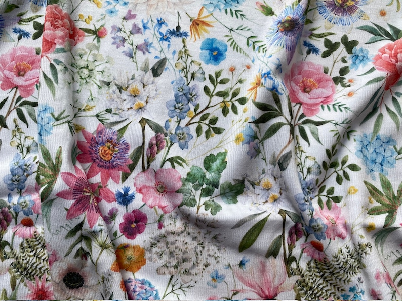 May include: A white fabric with a floral print featuring pink, blue, and purple flowers. The fabric has a wrinkled texture.