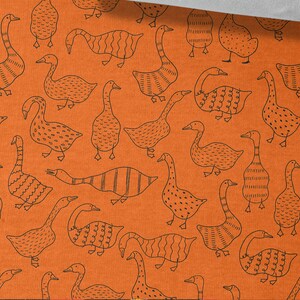 May include: Orange fabric with a repeating pattern of black geese. The geese are stylized and have different patterns on their bodies. The fabric is 50 cm / 19.70 inches wide.