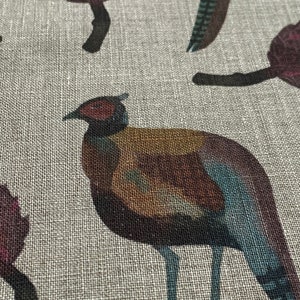 May include: A brown and blue pheasant with a red head is printed on a beige linen fabric. The pheasant is facing left and has a long tail.