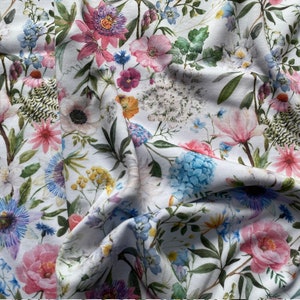 May include: White fabric with a floral print featuring pink, blue, and green flowers. The fabric is folded and draped, showcasing the intricate details of the floral pattern.