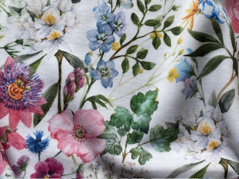 May include: White fabric with a floral print featuring pink, blue, and purple flowers. The fabric has a textured, linen-like appearance.