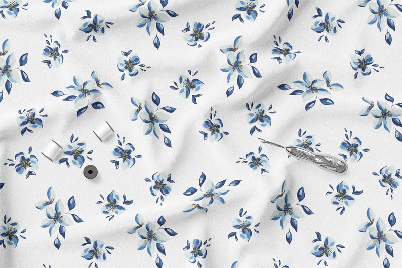 K&ouml;nnte beinhalten: Wei&szlig;er Stoff mit einem sich wiederholenden Muster aus blau-wei&szlig;en Blumenmustern. Das Bild enth&auml;lt drei Spulen wei&szlig;en Fadens, eine schwarze Spule und einen silbernen Nahttrenner. Geeignet f&uuml;r N&auml;h- oder Bastelprojekte.