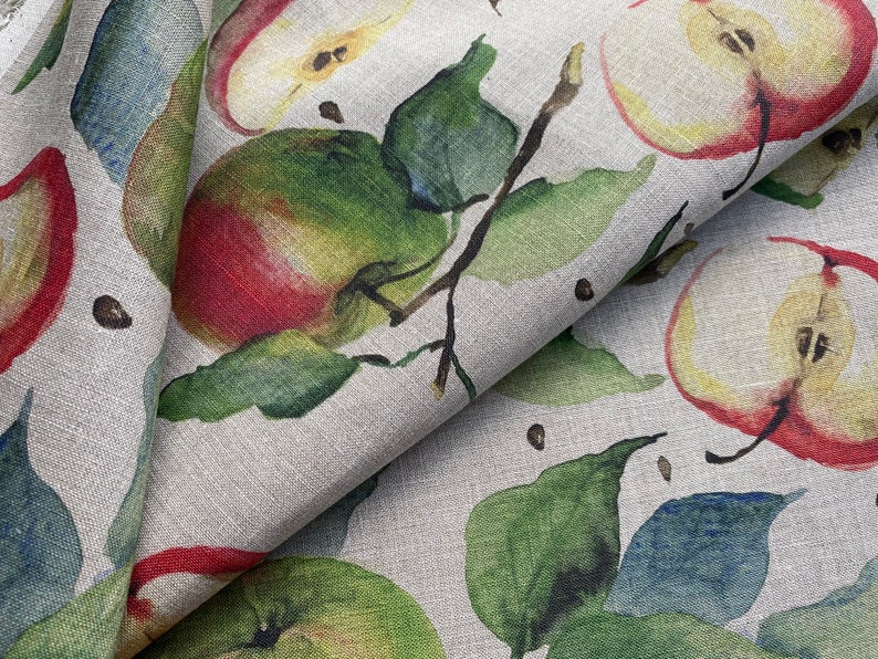 May include: A beige linen fabric with a repeating pattern of red and green apples, leaves, and black dots.