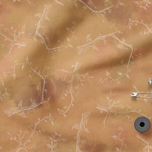 May include: A brown fabric with a white vine pattern. There are safety pins and a spool of thread on the fabric.