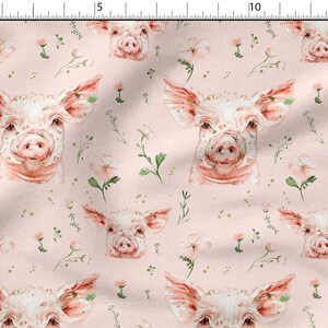 May include: A pink fabric with a repeating pattern of watercolor pig faces and delicate floral sprigs. The pigs have pink snouts and ears, and the flowers are white with pink centers.