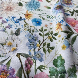 May include: A white fabric with a floral print featuring various flowers in shades of pink, blue, and yellow. The flowers are arranged in a random pattern and are surrounded by green leaves.