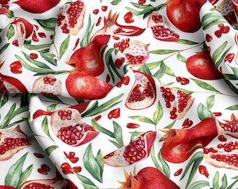 May include: A white fabric with a repeating pattern of red pomegranates and green leaves. The pomegranates are whole and cut open, showing the red seeds inside.