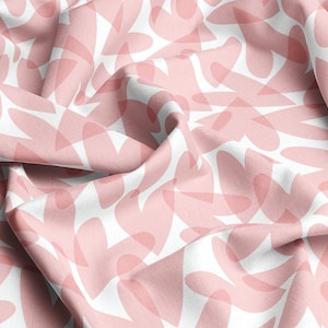 May include: Pink and white fabric with a repeating pattern of abstract shapes. The fabric is creased and has a soft, textured feel.
