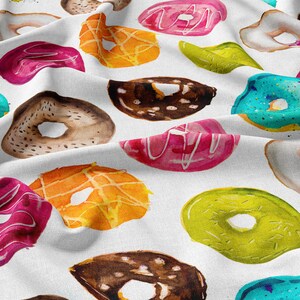 May include: A white fabric with a repeating pattern of colourful doughnuts. The doughnuts are glazed with pink, blue, green, orange, and brown frosting. Some doughnuts have sprinkles.