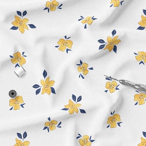 K&ouml;nnte beinhalten: Wei&szlig;er Stoff mit einem sich wiederholenden Muster aus gelben Blumen und marineblauen Bl&auml;ttern. Zwei Spulen wei&szlig;en Fadens und ein silberner Nahttrenner sind ebenfalls zu sehen. Geeignet f&uuml;r N&auml;h- oder Bastelprojekte.