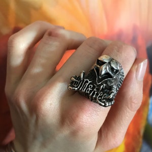 Peut inclure: Une bague en argent avec une tête d'aigle détaillée aux ailes déployées et le mot "Wild" inscrit sur la bande.