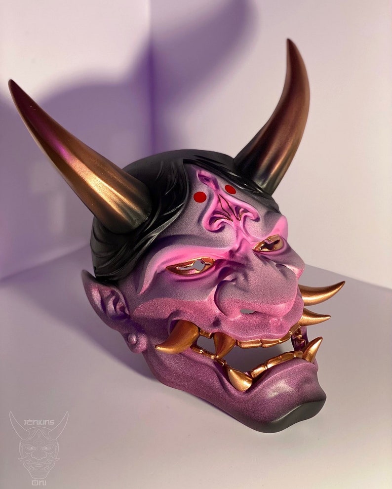 May include: A purple and gold Oni mask with a fierce expression. The mask has sharp teeth, horns, and a detailed design.