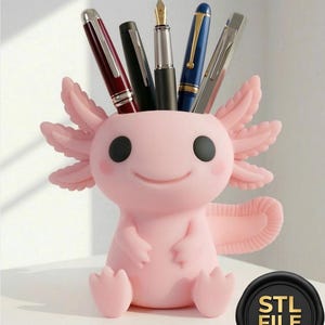 May include: A pink axolotl pen holder, holding pens of various colours. The holder has a smiling face and black eyes. The pens include burgundy, black, and blue. The holder is on a white surface.