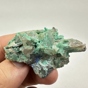 May include: A cluster of green malachite crystals with clear quartz crystals and a hint of blue azurite. The crystals are embedded in a gray matrix.