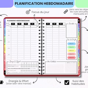 May include: An open spiral-bound weekly planner with a red cover. The pages feature a grid layout for daily scheduling, sections for daily focus, habit tracking, project lists, and energy and effort logs. The planner includes colorful tabbed dividers for months and projects, with text in French throughout the layout.