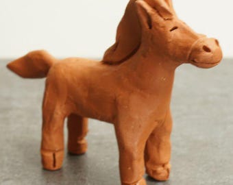 May include: A small, handcrafted clay horse figurine in a warm brown hue. The horse stands with four legs, a flowing mane, and a small tail. The figurine is a simple, yet charming representation of a horse.