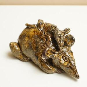 May include: A ceramic sculpture of a mother rat with a baby rat on its back. The sculpture is brown with darker brown and gold accents. The rat's features are detailed, including the eyes, ears, and nose.