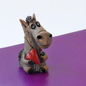 May include: A ceramic figurine of a gray donkey holding a red heart. The donkey has large eyes and a friendly expression.