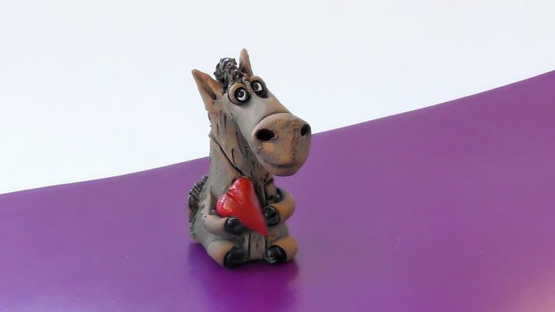 May include: A ceramic figurine of a gray donkey holding a red heart. The donkey has large eyes and a friendly expression.