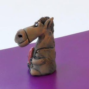 May include: A brown ceramic donkey figurine with a red tongue sticking out. The donkey is sitting down and has a whimsical expression.