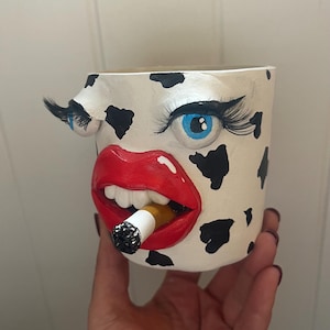 Divertida y extraña maceta con forma de cara, con ojos, pestañas, cigarrillo y labios.