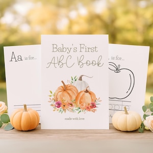 Peut inclure: Trois cartes avec des illustrations et du texte sur le thème de l'automne. La carte centrale indique "Baby's First ABC Book" avec des citrouilles et des motifs floraux. Les autres cartes ont les lettres "Aa" et un contour de pomme. De petites citrouilles et des fleurs sont au premier plan.