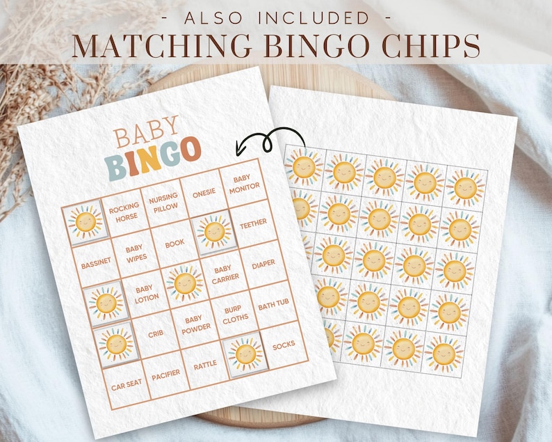 May include: A printable baby shower bingo card with a colourful sun design. The card features a 5x5 grid with squares containing baby-related items such as a rocking horse, nursing pillow, onesie, baby monitor, and teether. The card is designed for a baby shower game.