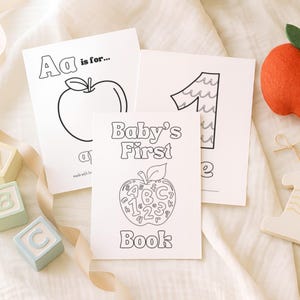 May include: A collection of educational baby items, including coloring pages with the text "Baby's First Book", "A is for...", and the number "1". Also featured are wooden blocks with letters, a felt apple, and a wooden number one.