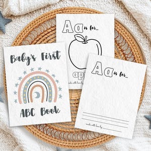 Boho rainbow ABC coloring book pages for baby shower. Printable baby alphabet book with 'A is for...' pages to color. A unique guest book alternative and 1st birthday keepsake gift. Displayed on a woven tray with soft blankets and star decorations.