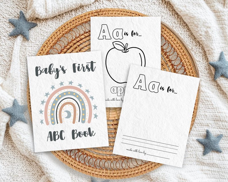 Boho rainbow ABC coloring book pages for baby shower. Printable baby alphabet book with 'A is for...' pages to color. A unique guest book alternative and 1st birthday keepsake gift. Displayed on a woven tray with soft blankets and star decorations.