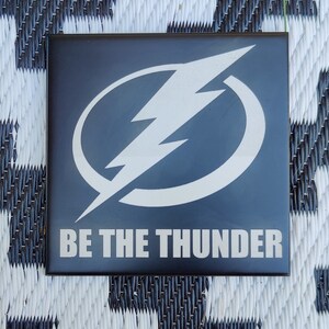 May include: A black square tile with a white lightning bolt in a circle and the text "BE THE THUNDER" in white.