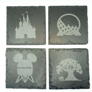 May include: Set of four black slate coasters with engraved images of iconic Disney World attractions: Cinderella's Castle, Spaceship Earth, Mickey Mouse's head, and the Tree of Life.