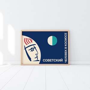 May include: A vintage-style poster with a blue background and a white circle with a teal half-circle. The poster features a stylized drawing of a person's head with a red and white striped helmet. The text on the poster reads "Советский Человек в Космосе".