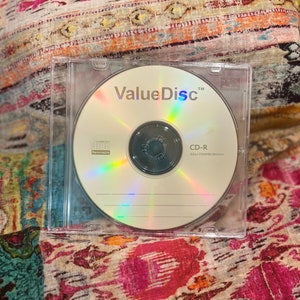 Puede incluir: Un disco CD-R plateado en una caja de plástico transparente. El disco está etiquetado como "ValueDisc™" y tiene el texto "CD-R 52x/700MB/80min" impreso en él.