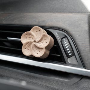 May include: A brown wooden flower-shaped car air freshener hanging from a car's air vent.