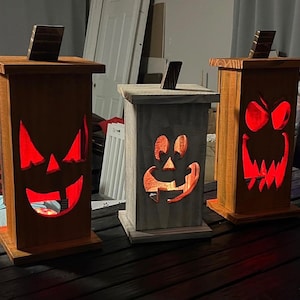 May include: Five wooden jack-o'-lantern candle holders with different facial expressions. The candle holders are lit with red, orange, and purple lights.
