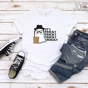 May include: White t-shirt with a black and white illustration of a ghost wearing a hat and glasses. The text "It's Tricky Tricky Tricky Tricky" is printed on the shirt.